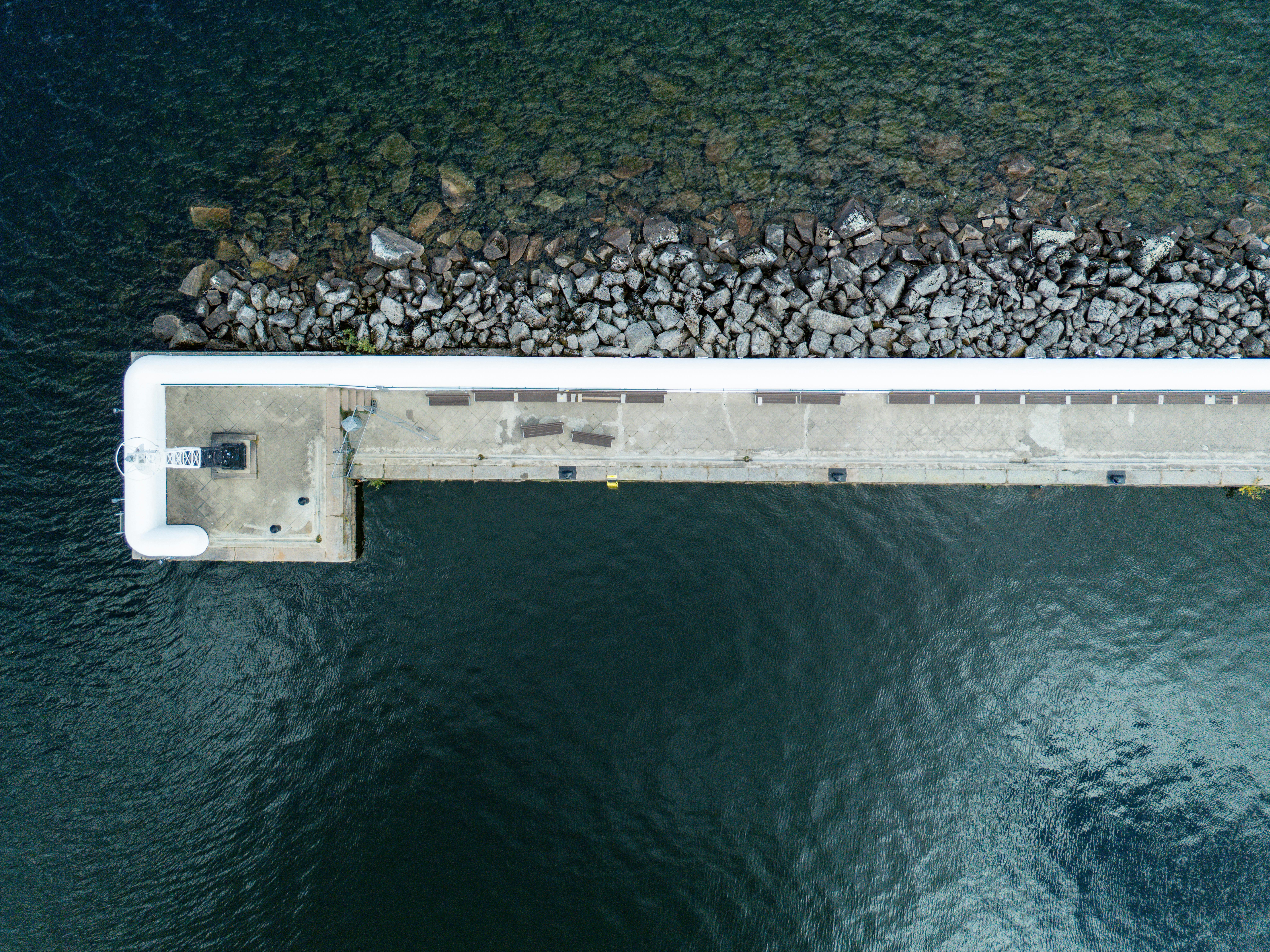 Drohnenaufnahme eines Piers, der in einen klaren, blauen, von Felsen gesäumten See in Jönköping, Schweden, hineinragt.