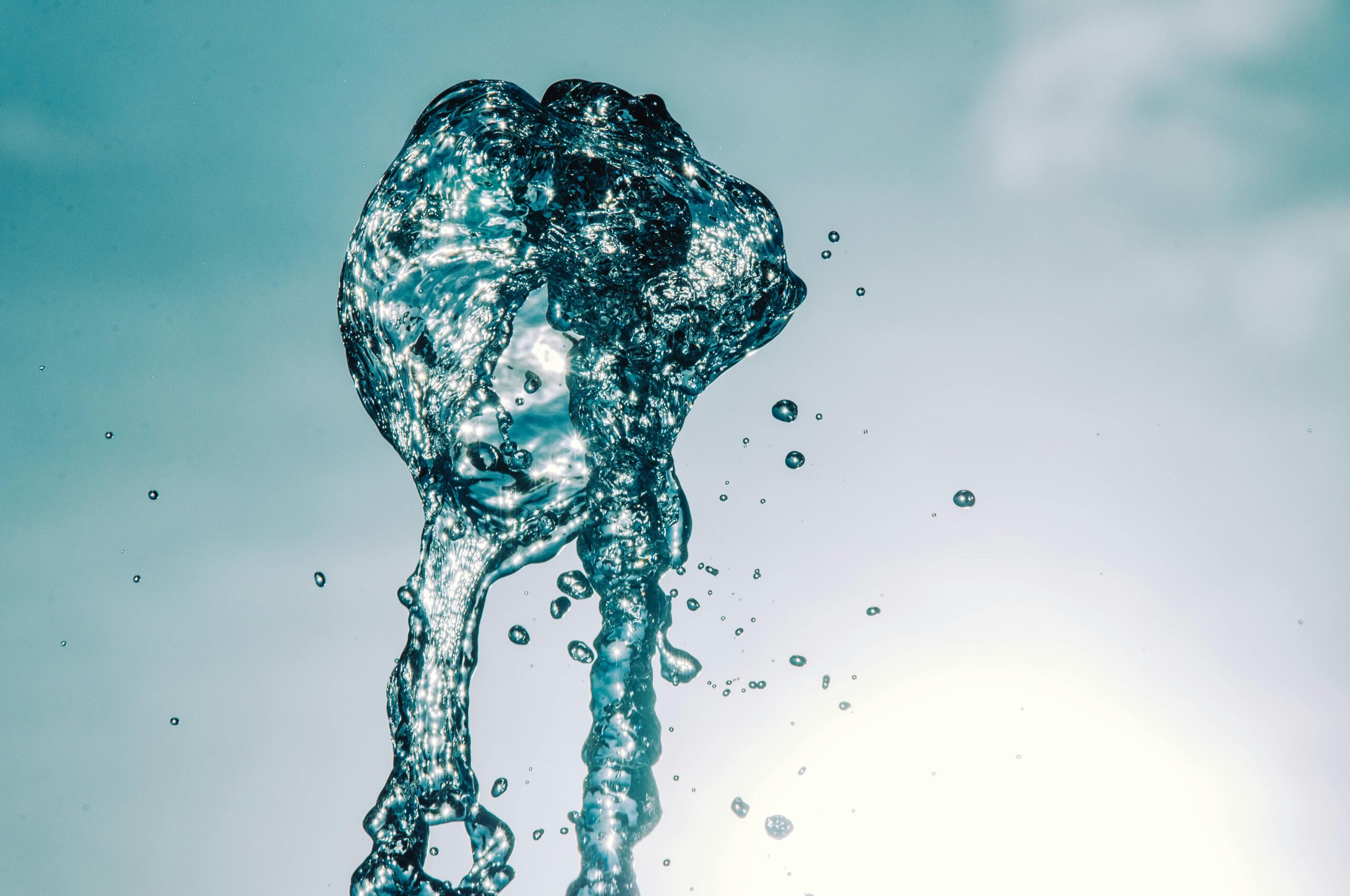 Nahaufnahme eines Wasserspritzers in der Luft vor hellem Himmel, die Bewegung und Transparenz einfängt.