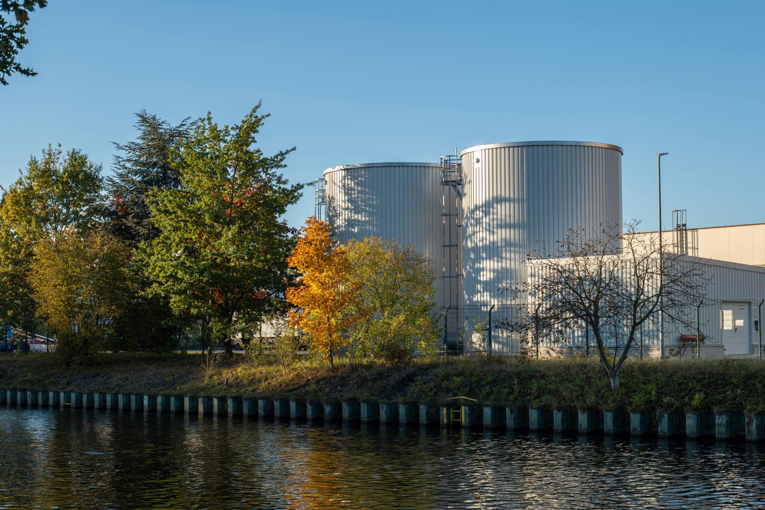 Ein malerischer Blick auf zwei große Silos an einem baumbestandenen Flussufer an einem klaren Tag.